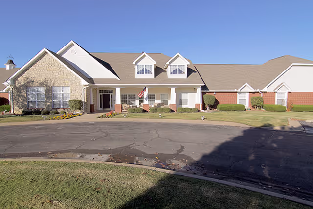 Front exterior of a single-story senior living facility with a covered entrance, American flag, and circular driveway.