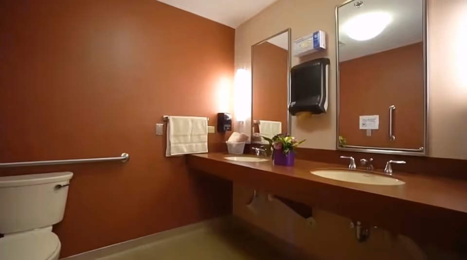 Clean bathroom with dual sinks, mirrors, towel rack, and toilet in a senior living facility.