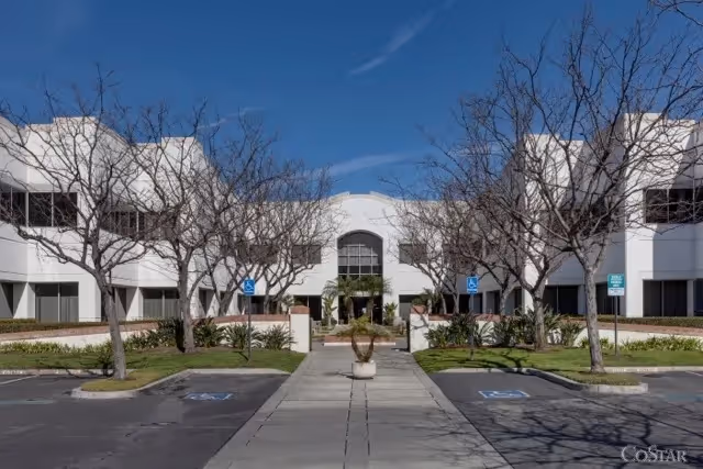 Wide view of a white modern senior living building with a central entrance and trees.