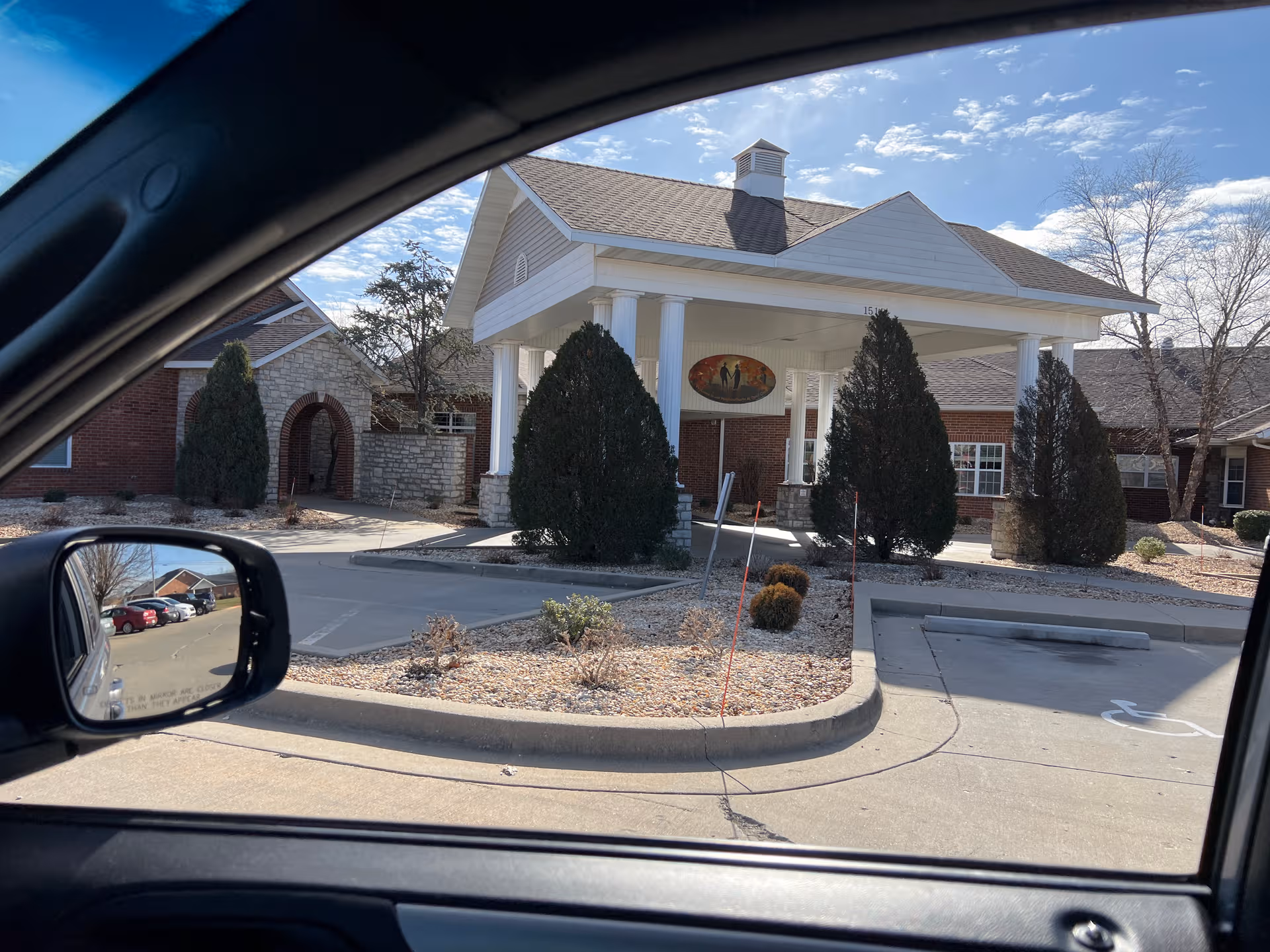 Front of a senior living facility with a covered entrance and landscaped driveway.