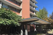 Multi-story senior living facility exterior with a covered entrance, brick facade, and greenery.