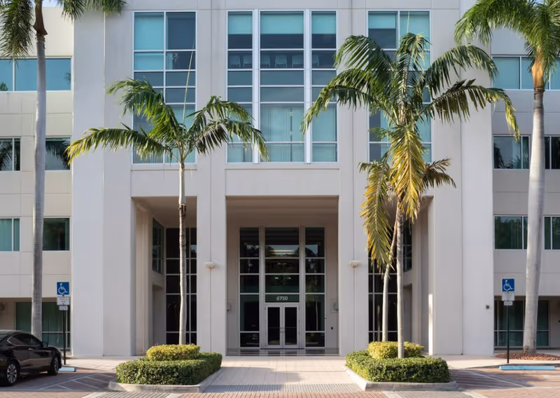 Modern building facade with glass entrance, palm trees, and accessible signage.