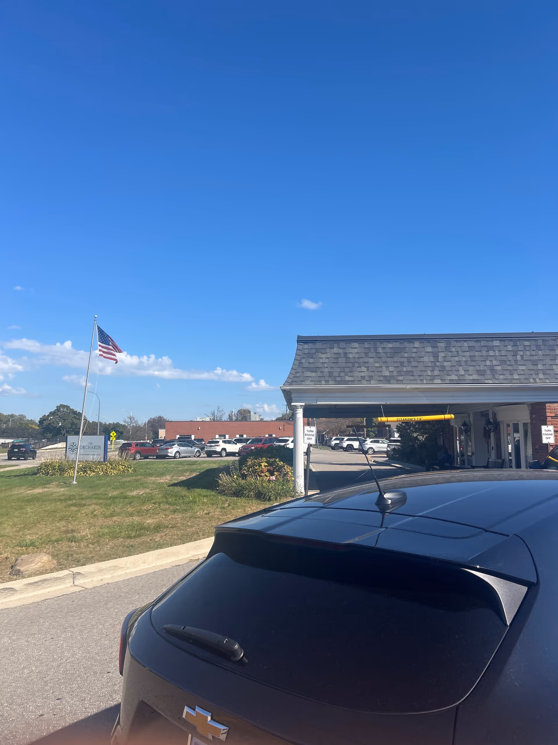 Exterior view of Advantage Living Center Harper Woods with parking lot, cars, and flagpole.