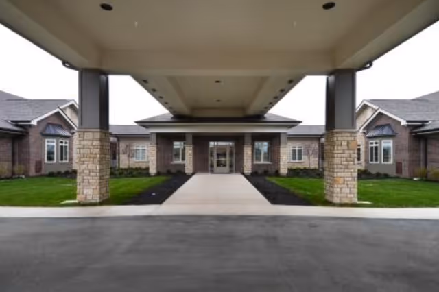 Covered drop-off entrance to a brick senior living facility with a paved walkway.