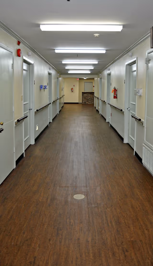 Long brightly lit corridor inside a senior living facility with doors and handrails