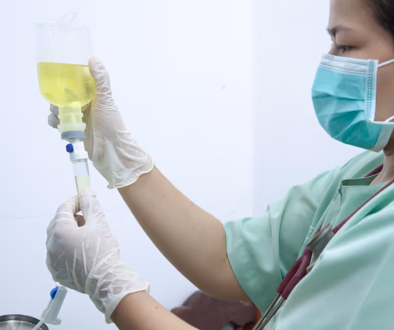 Nurse in mask and gloves prepares an IV drip bag.