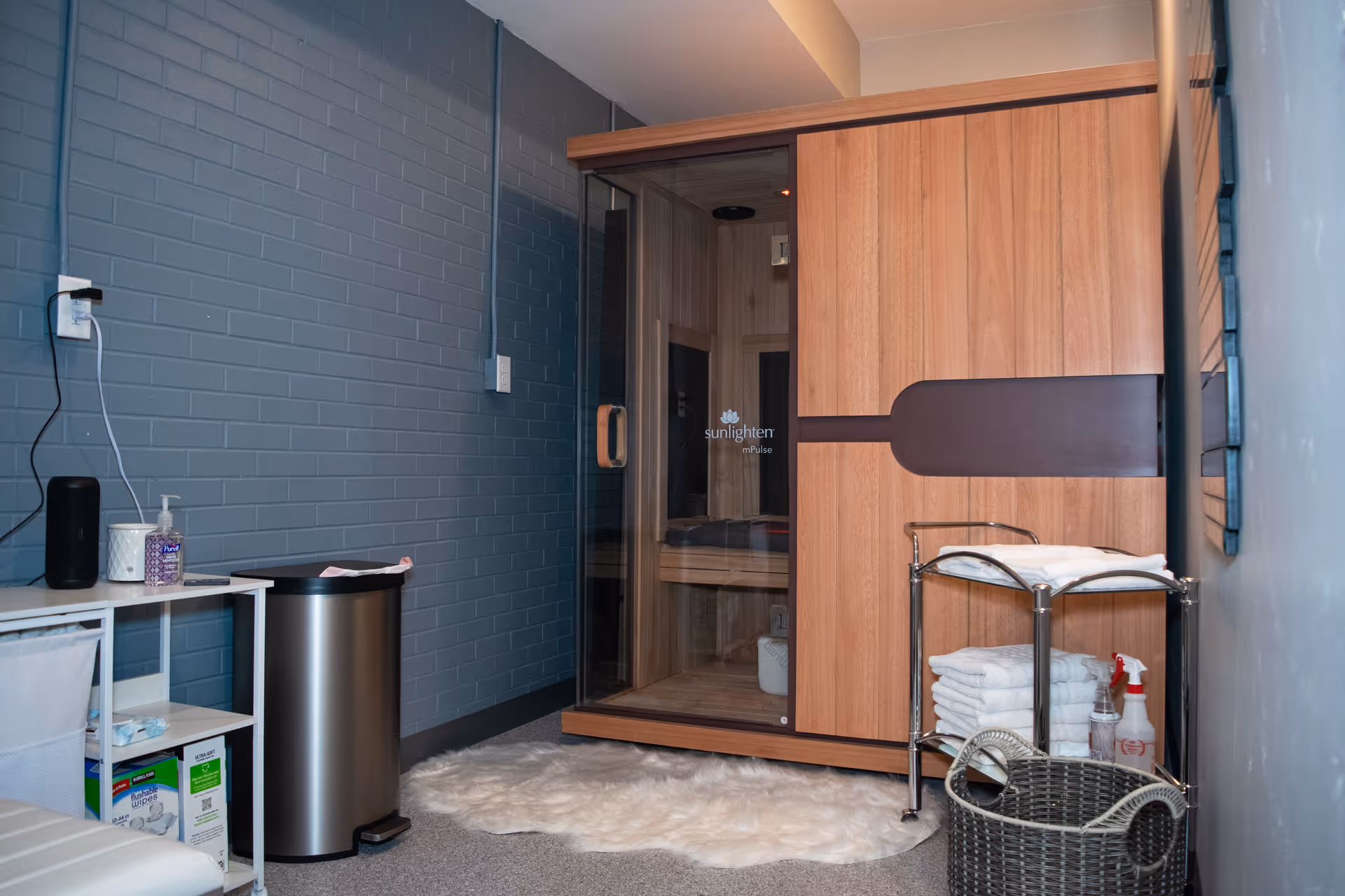 Blue brick-walled therapy room with a wooden sauna and towel cart.