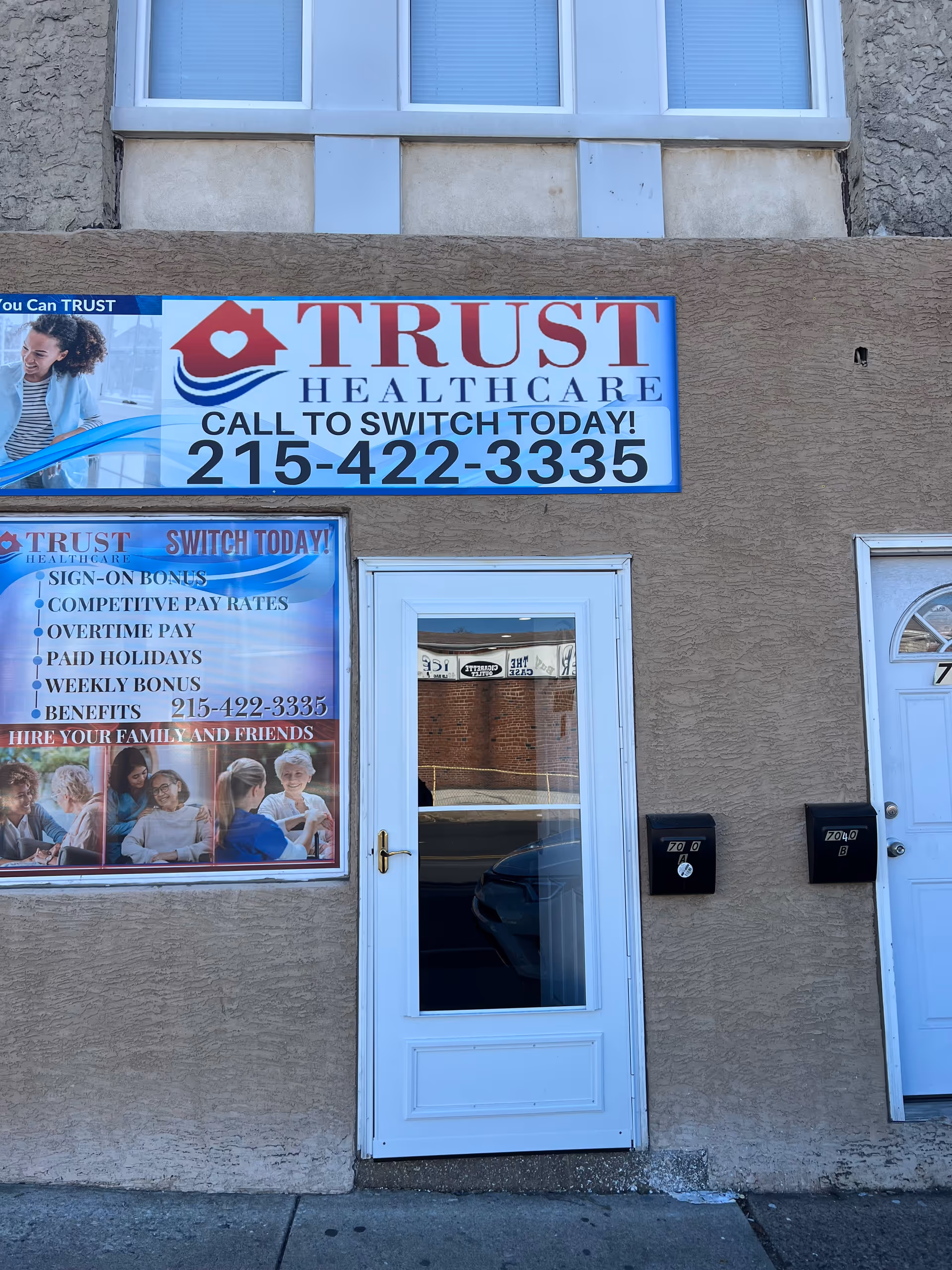 Exterior of Trust Healthcare building with large sign, banners, and a glass front door.