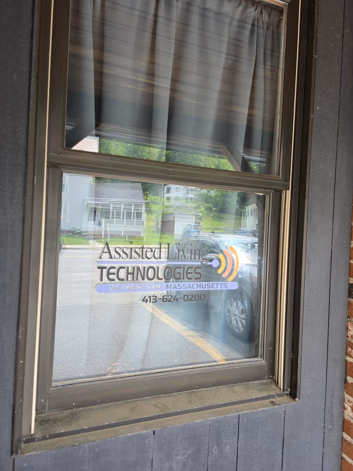 Window showing street reflection and logo reading Assisted Living Technologies of Western Massachusetts.