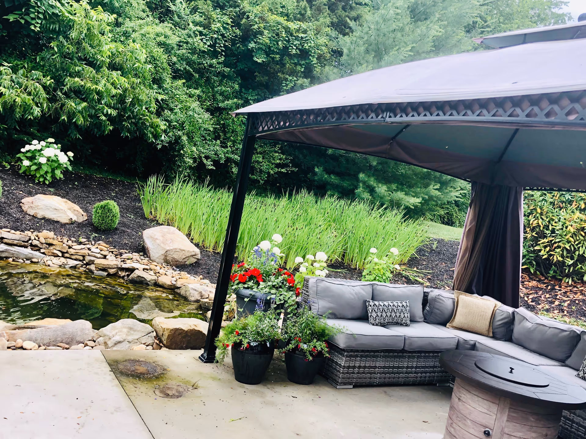 Outdoor patio with cushioned seating under a canopy beside a pond.