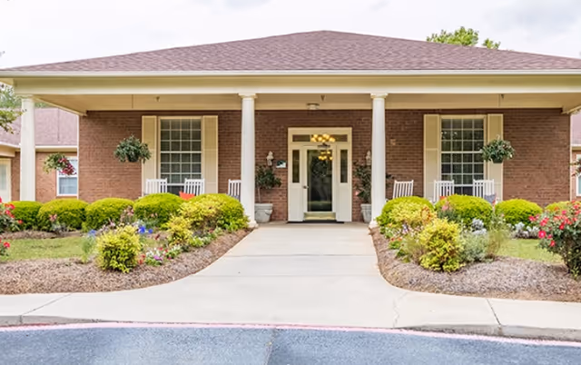 Front view of a brick senior living facility with columns, glass door, and landscaped walkway.