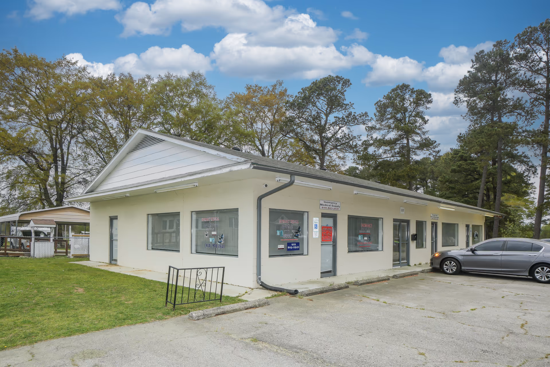 Single-story beige building exterior with windows, a small parking lot, and trees nearby.