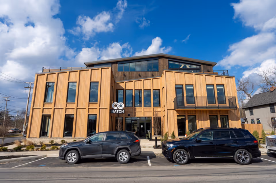 Modern wooden building exterior with large windows and parked cars in front.