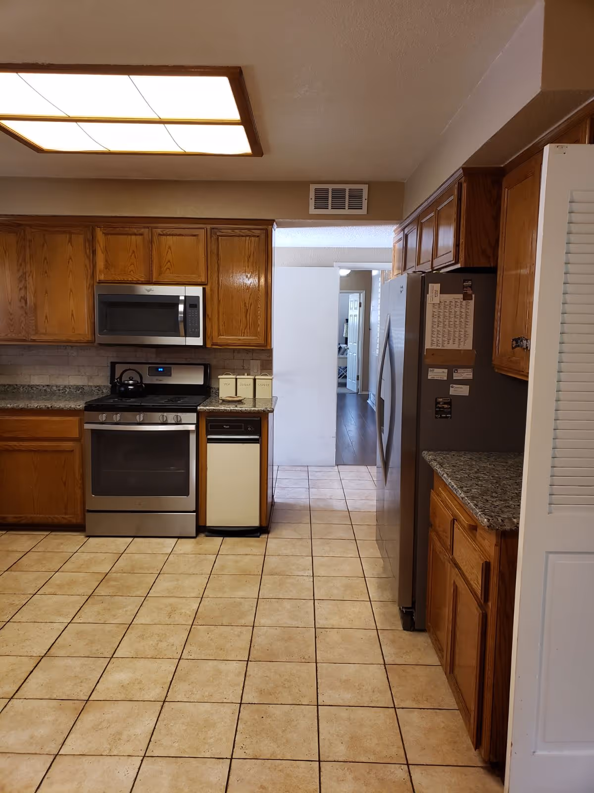 Residential kitchen with wooden cabinets, stainless appliances, and tiled floor.