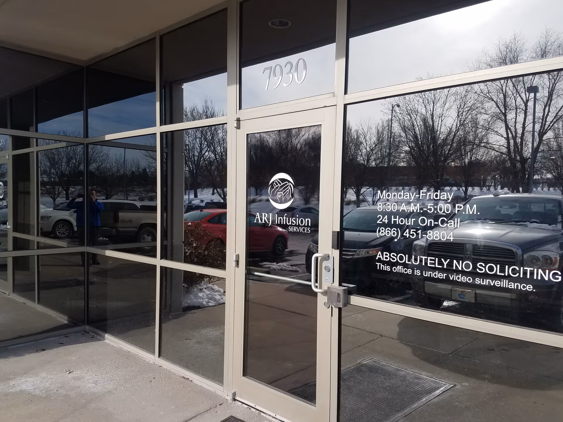Glass-front building entrance with ARJ Infusion Services signage and reflected parked cars in the glass.