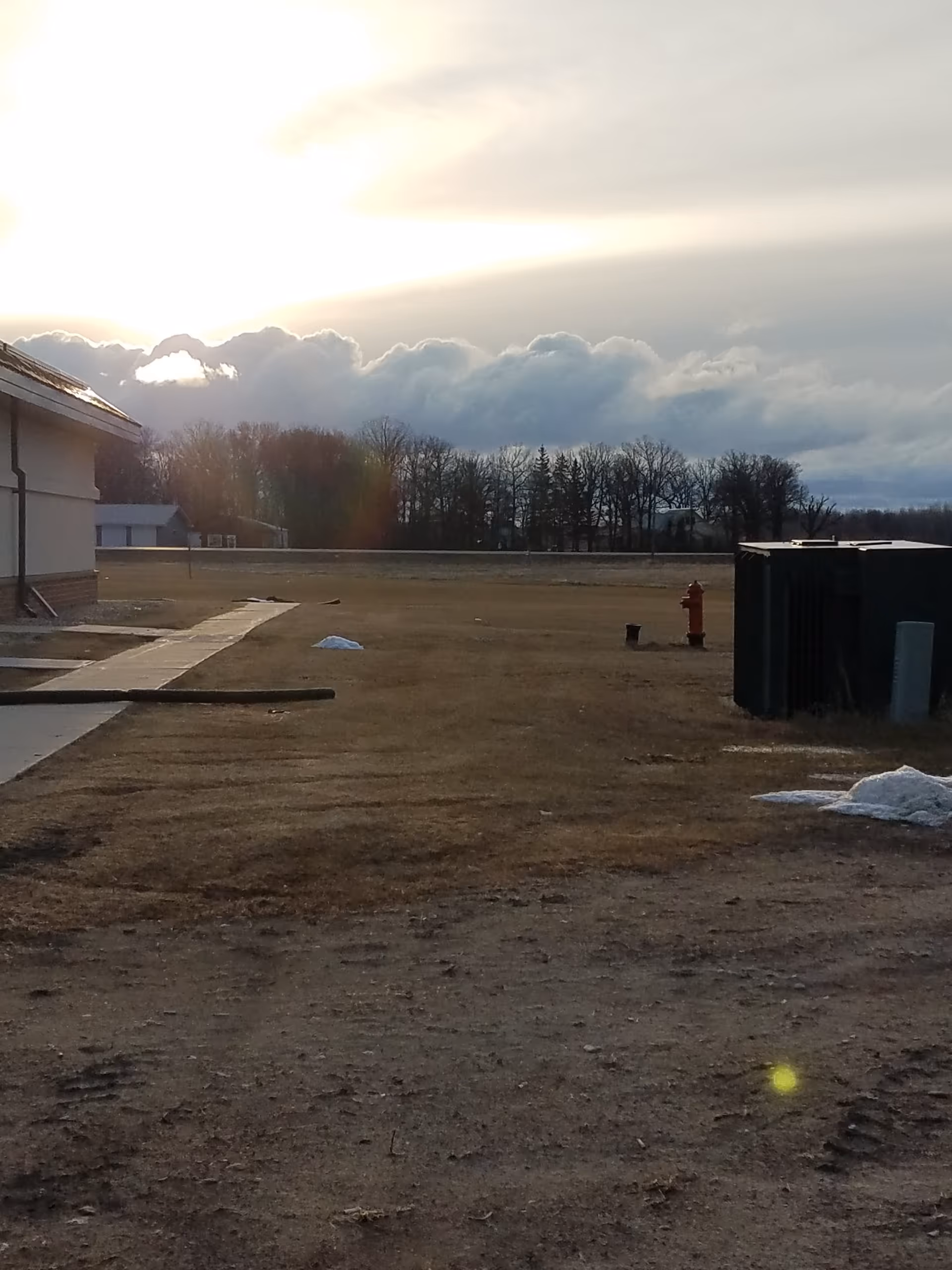Exterior view of a barren facility yard with a building, hydrant, and dumpster.