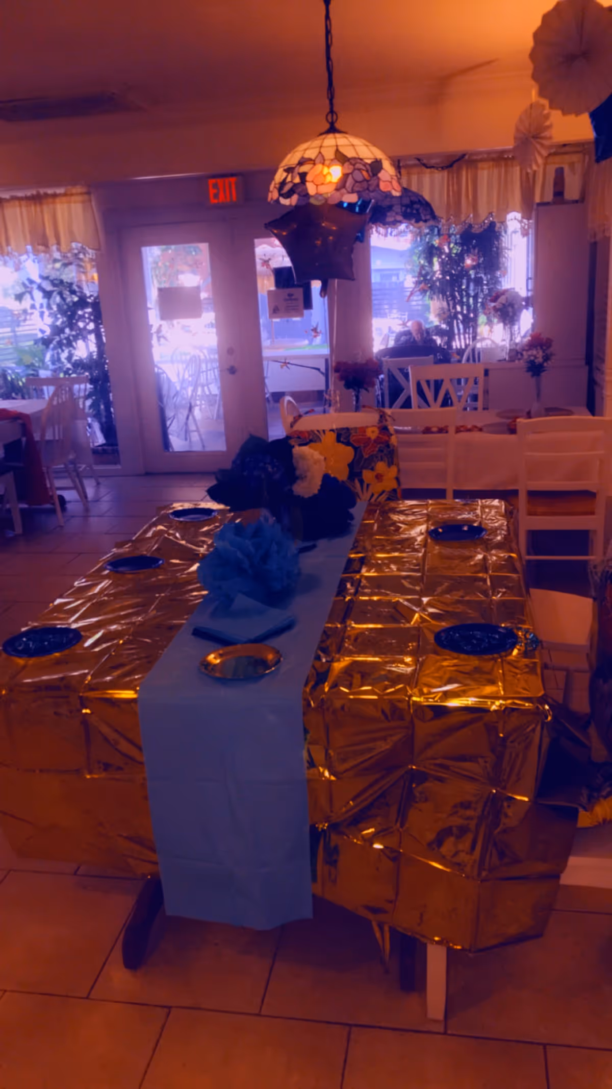 Decorated dining room with a long gold table, blue runner, and floral centerpiece.