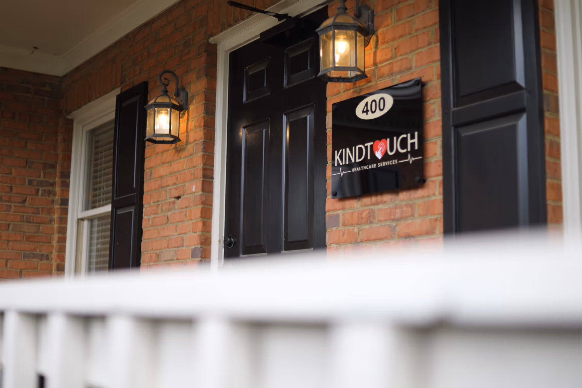 Brick building entrance with black door, hanging lanterns, and KindTouch Healthcare Services sign.