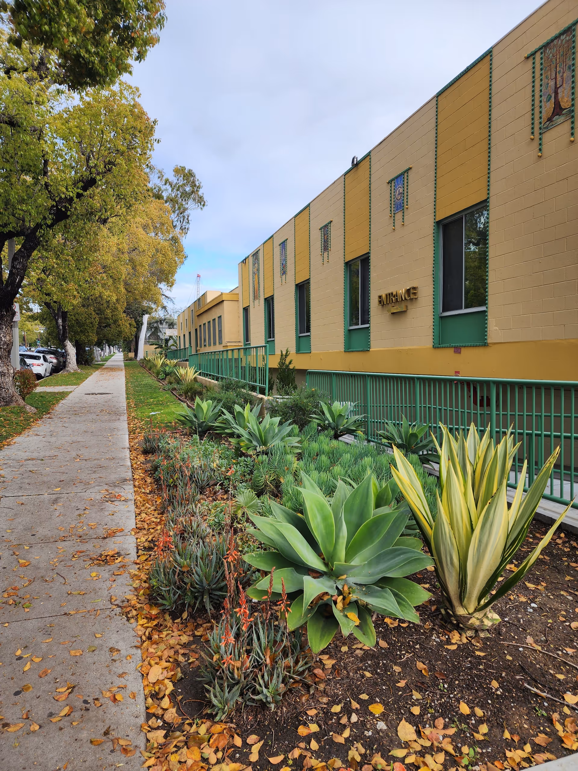 Exterior view of a beige and green facility with a walkway and succulent garden.