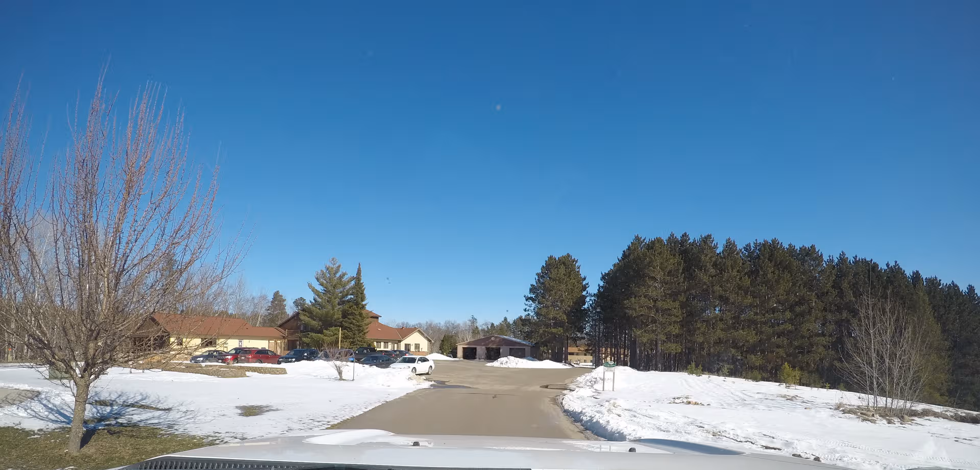 Snowy driveway leads to Shiloh Assisted Living front with parked cars and evergreen trees.