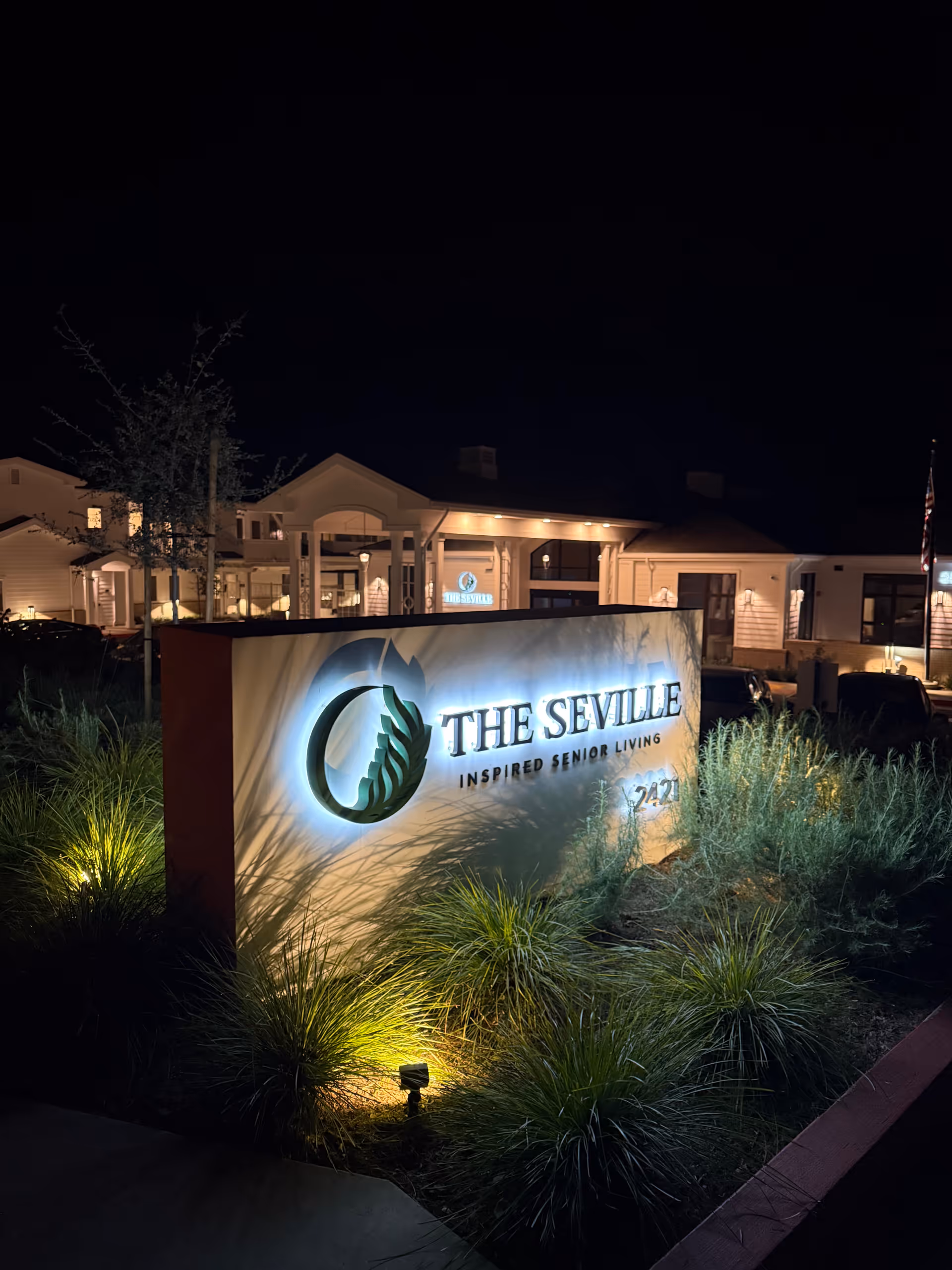 Nighttime exterior view of The Seville sign and front entrance with illuminated landscaping.