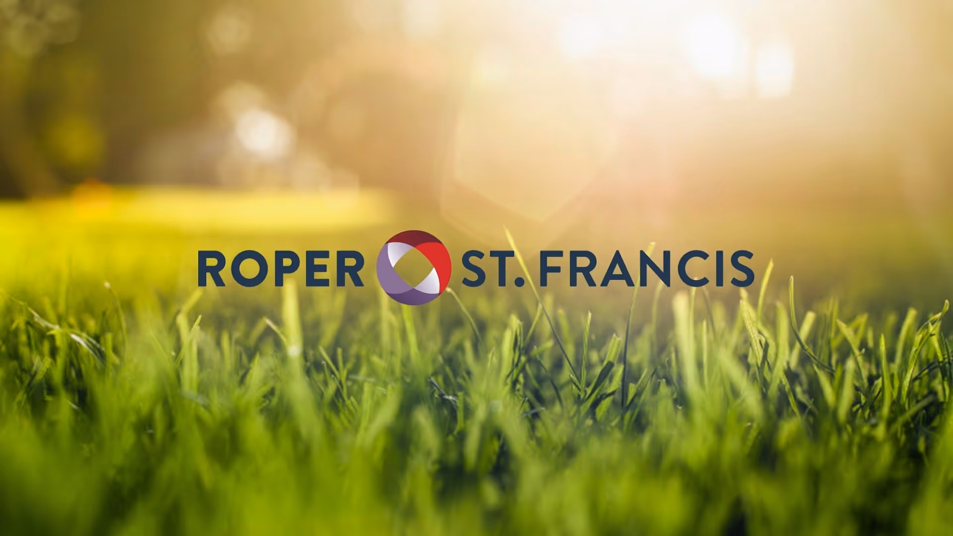 Close-up view of green grass with warm sunlight and Roper St. Francis logo in center.