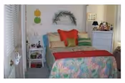 Brightly decorated senior living bedroom featuring a colorful quilt, pillows, dresser, and plants.