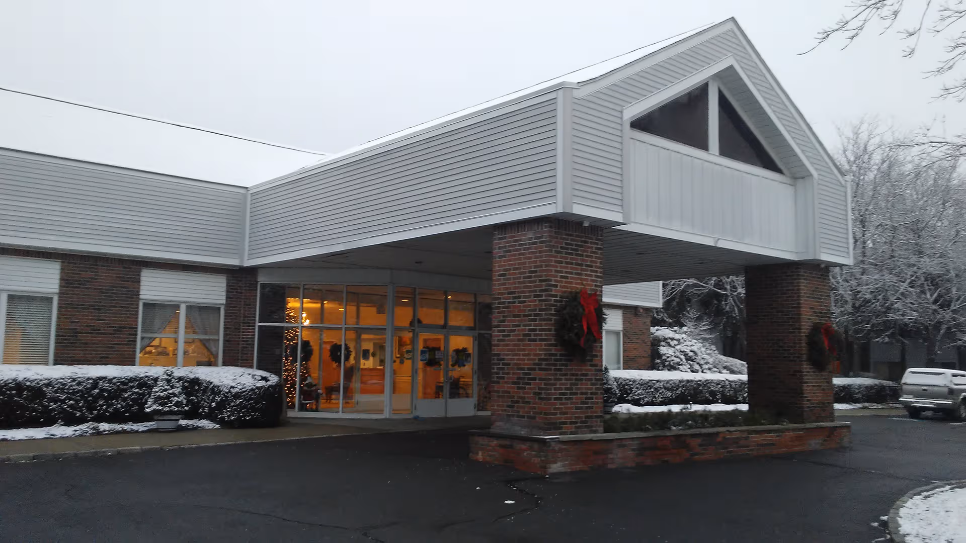 Winter scene at Wilton Meadows Nursing and Rehabilitation entrance with brick pillars and glass doors.
