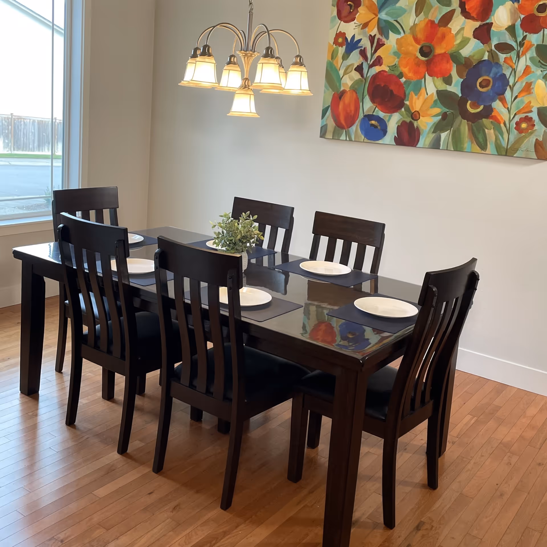 Dark wood dining table with eight chairs, plates, and colorful wall art in a dining room.