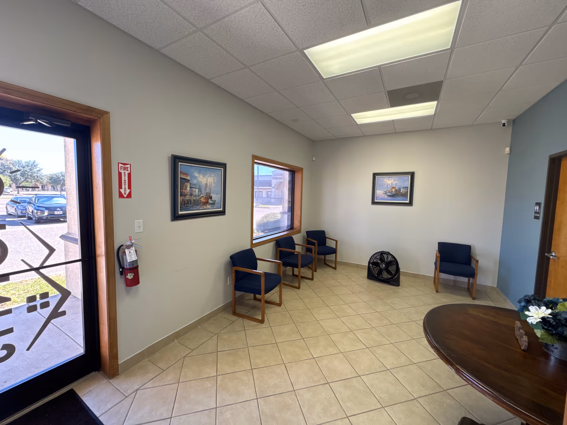 Waiting area with several blue chairs along the wall and a curved wooden table.