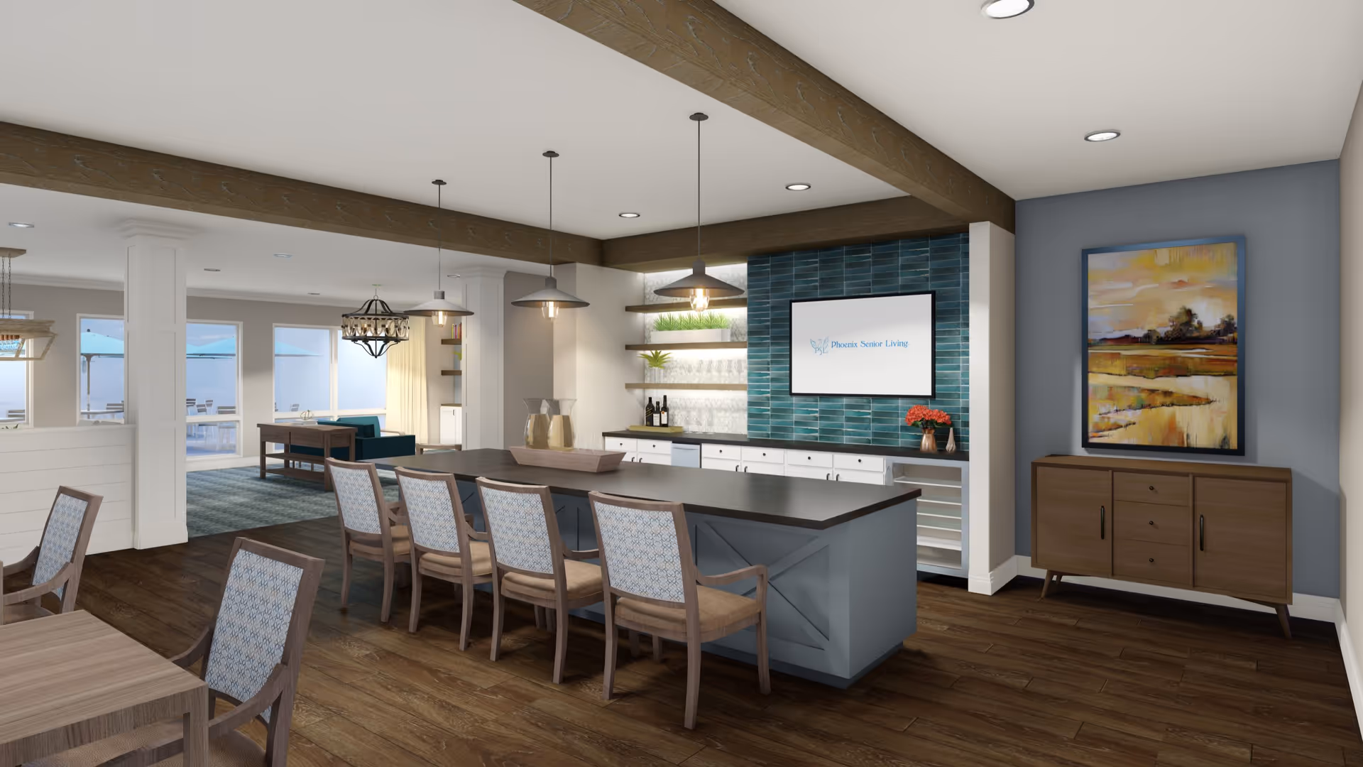A modern communal dining and lounge area with a large island table surrounded by chairs, pendant lights hanging from the ceiling, a sideboard with a colorful abstract painting above it, and a wall-mounted screen displaying 'Phoenix Senior Living'. The room has wooden floors, exposed wooden beams on the ceiling, and large windows letting in natural light.