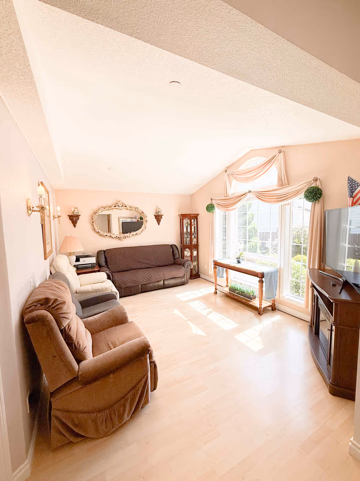 Bright pastel living room with recliners, sofa, and large windows in a senior facility.
