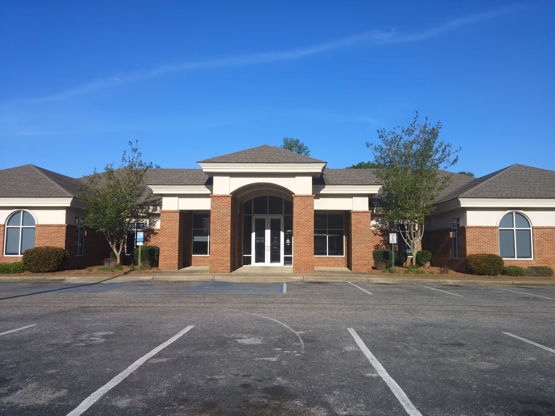 Exterior view of a brick health department building with a central arch entrance and parking.