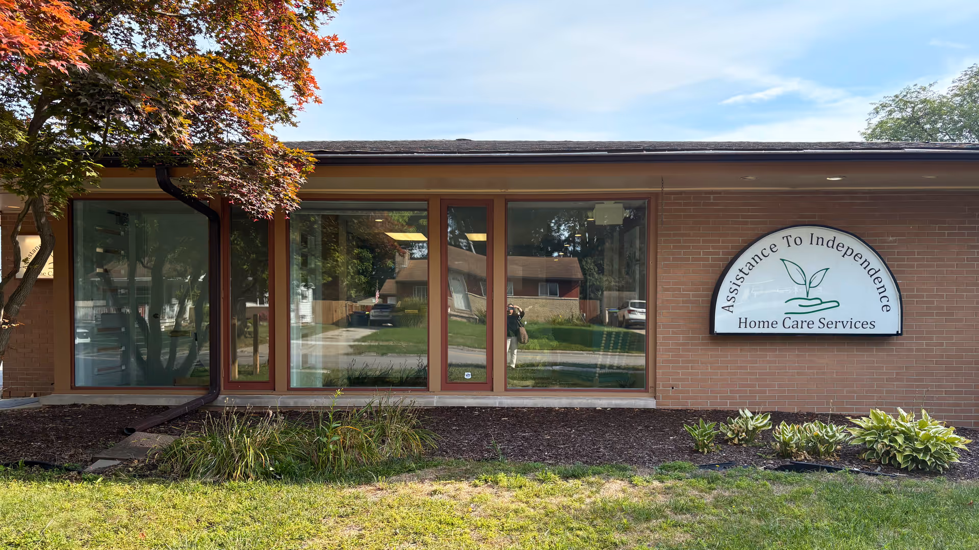 Brick building with large windows and a curved sign reading Assistance To Independence Home Care Services.