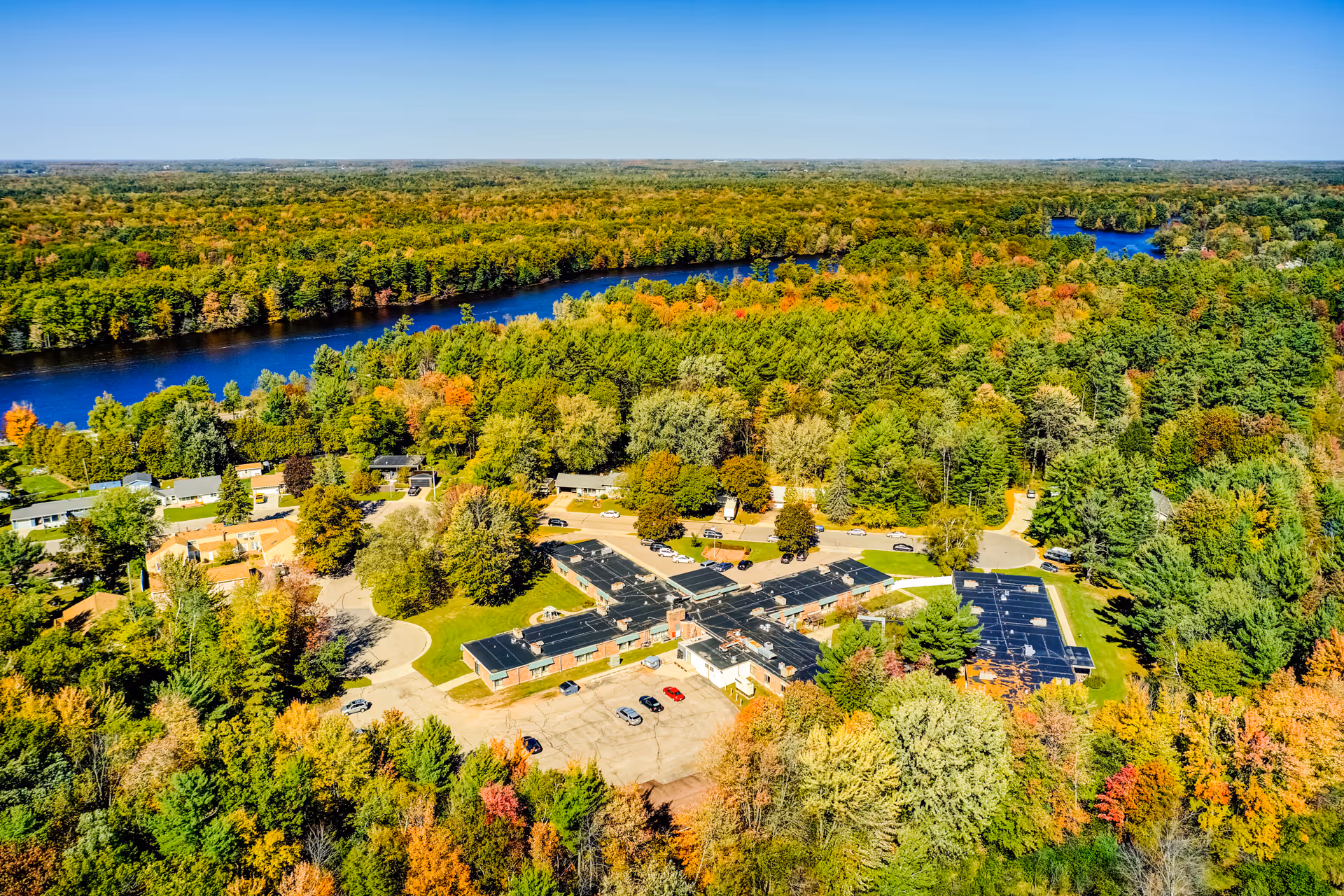 Aerial view of a senior living facility complex surrounded by dense trees and a winding river.