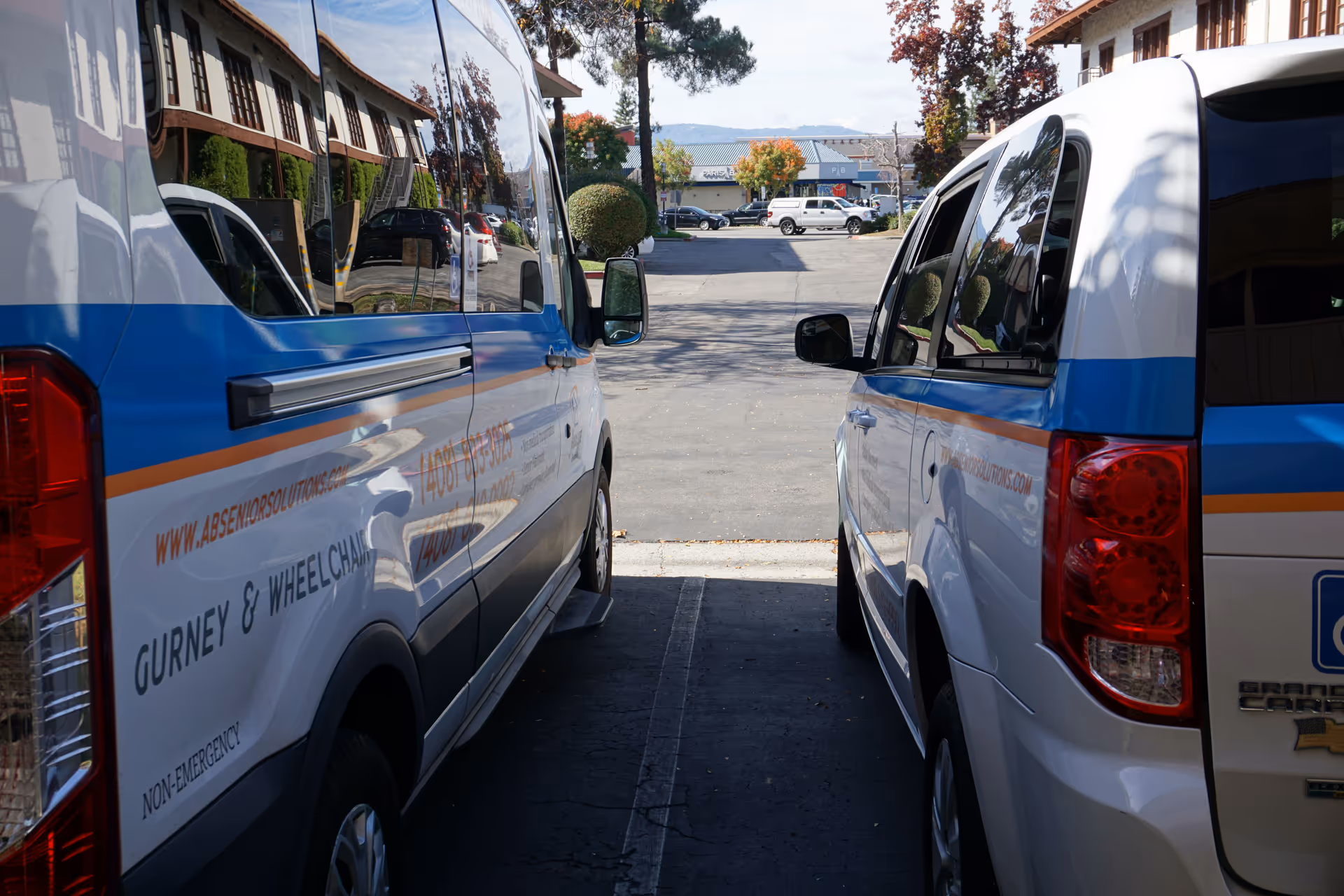 Two white and blue senior transport vans parked outside a facility with a building in background.