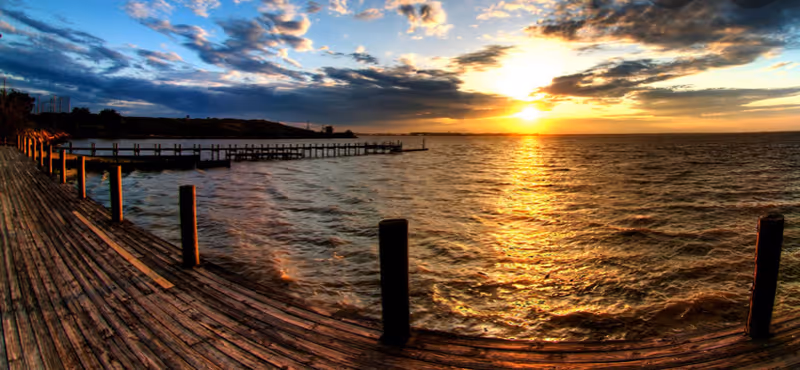 Sunset over a wooden pier beside calm water, with a glowing horizon.
