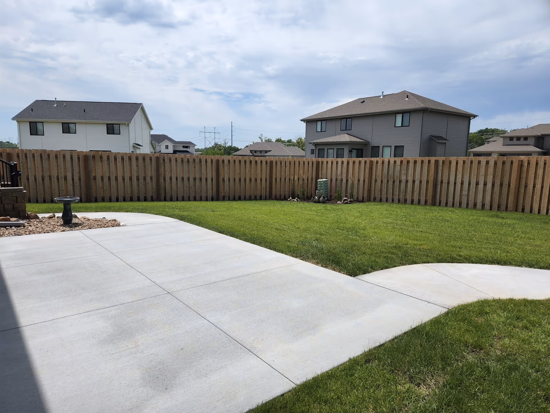 Backyard with green lawn, wooden fence, and concrete patio between neighboring houses.