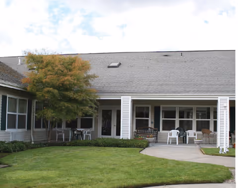 Exterior view of a single-story memory care facility with a grassy yard and patio seating.