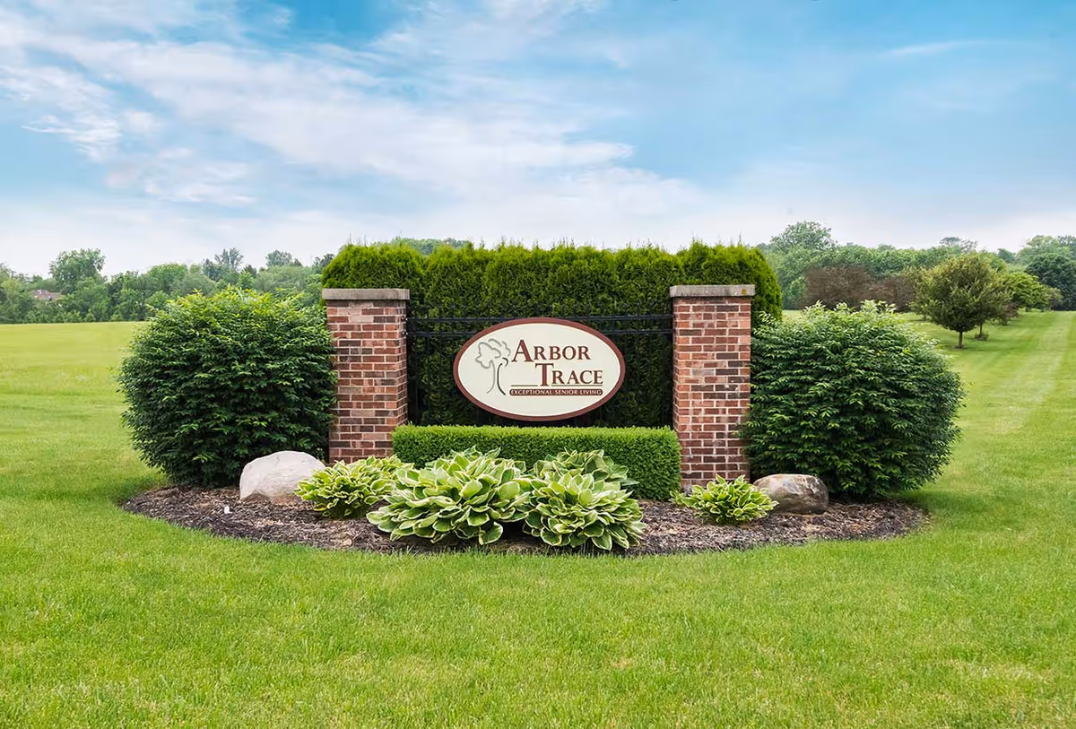 Landscaped entrance sign for Arbor Trace mounted between brick pillars amid shrubs and a manicured lawn.