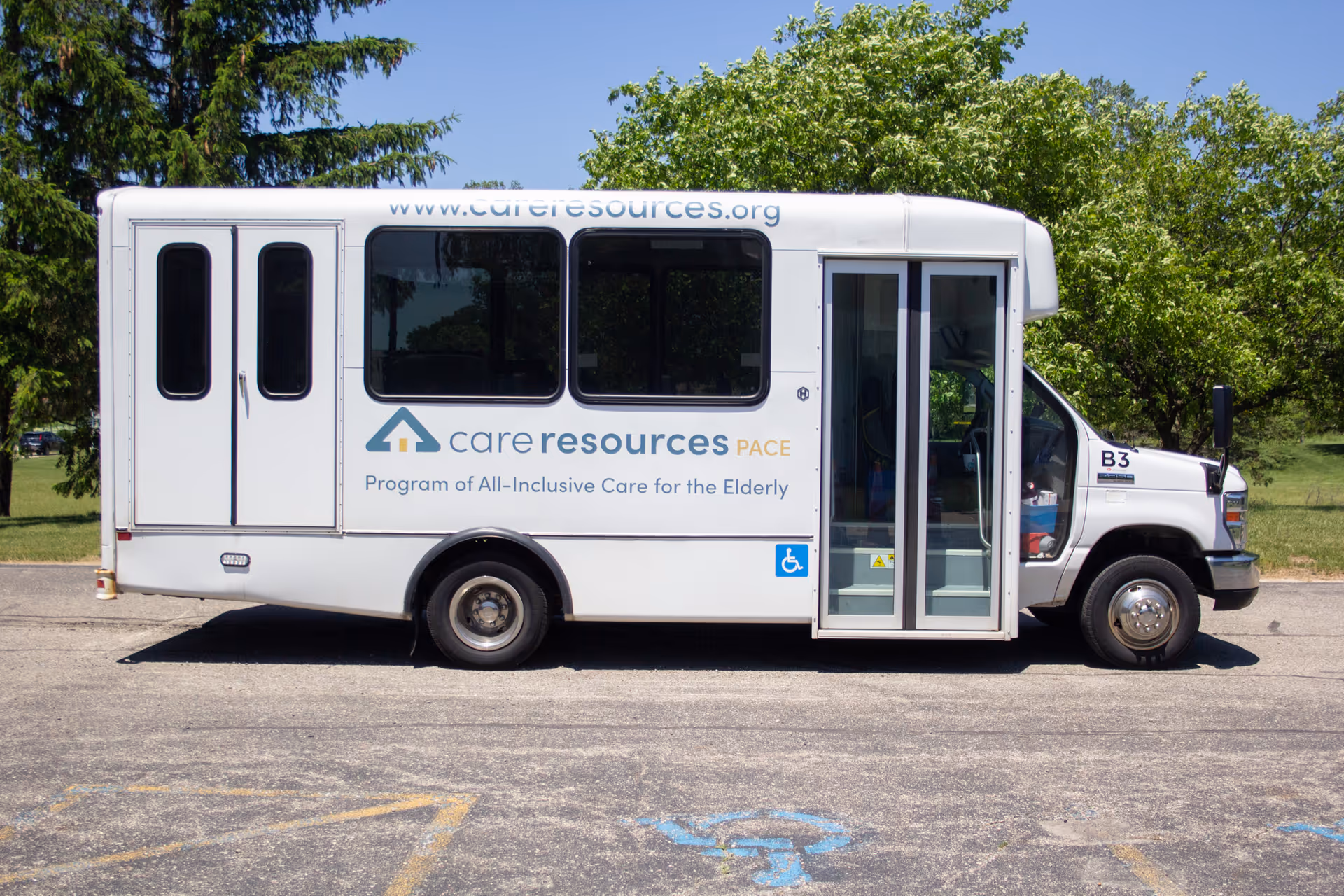 White bus with Care Resources PACE branding parked on a paved lot beside trees