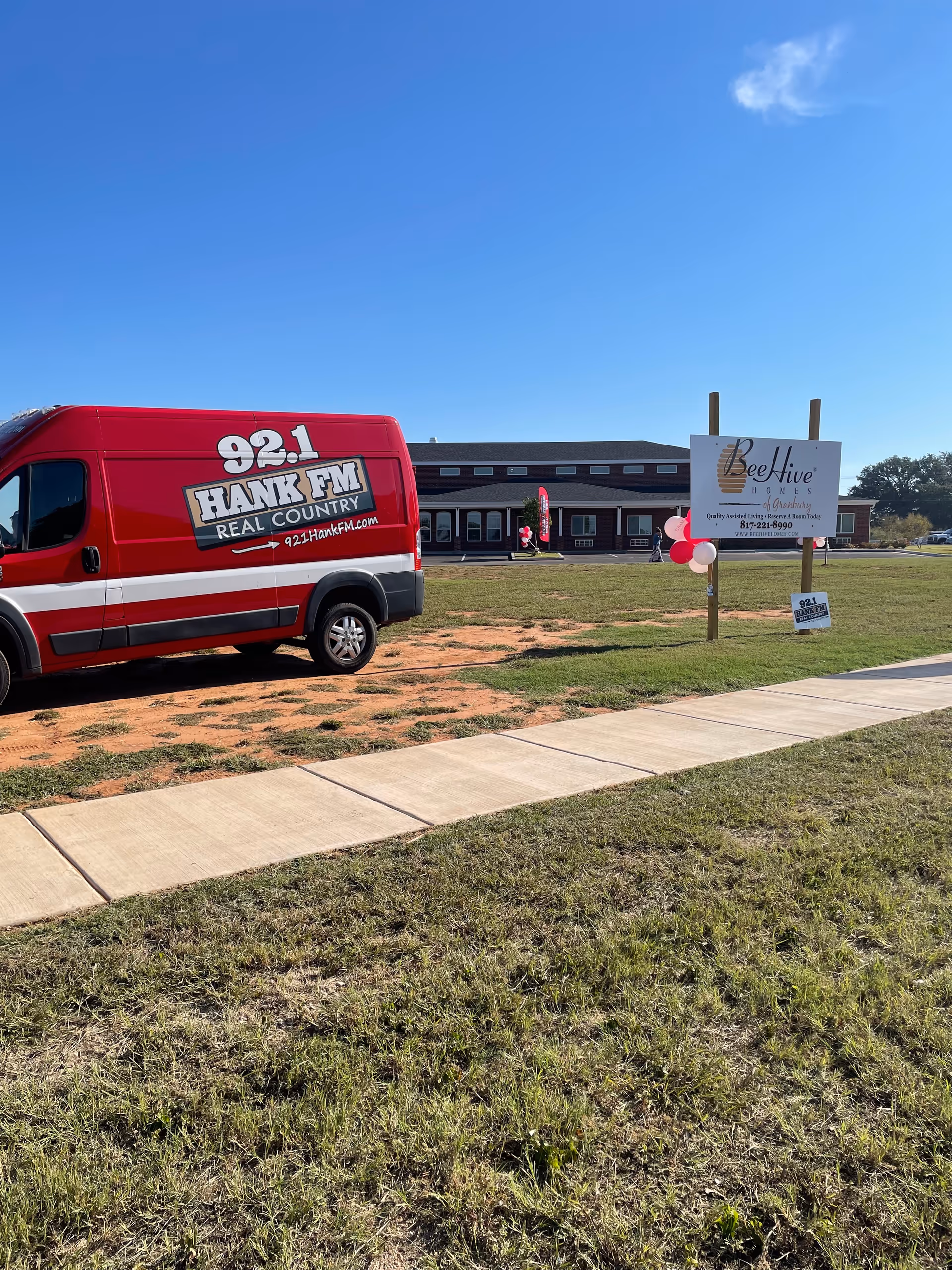 Red van parked in front of BeeHive Homes Granbury building with sign and balloons