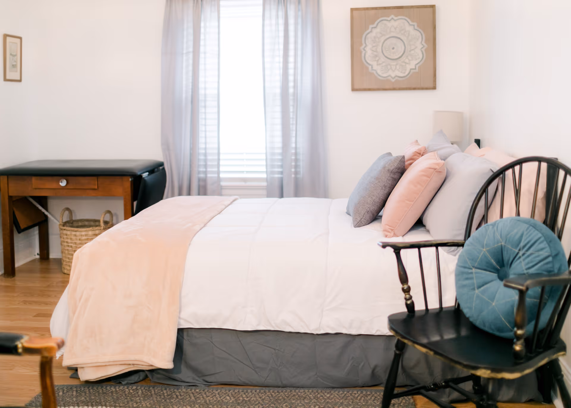 A neatly made bedroom with a bed, pillows, and a window with sheer curtains.