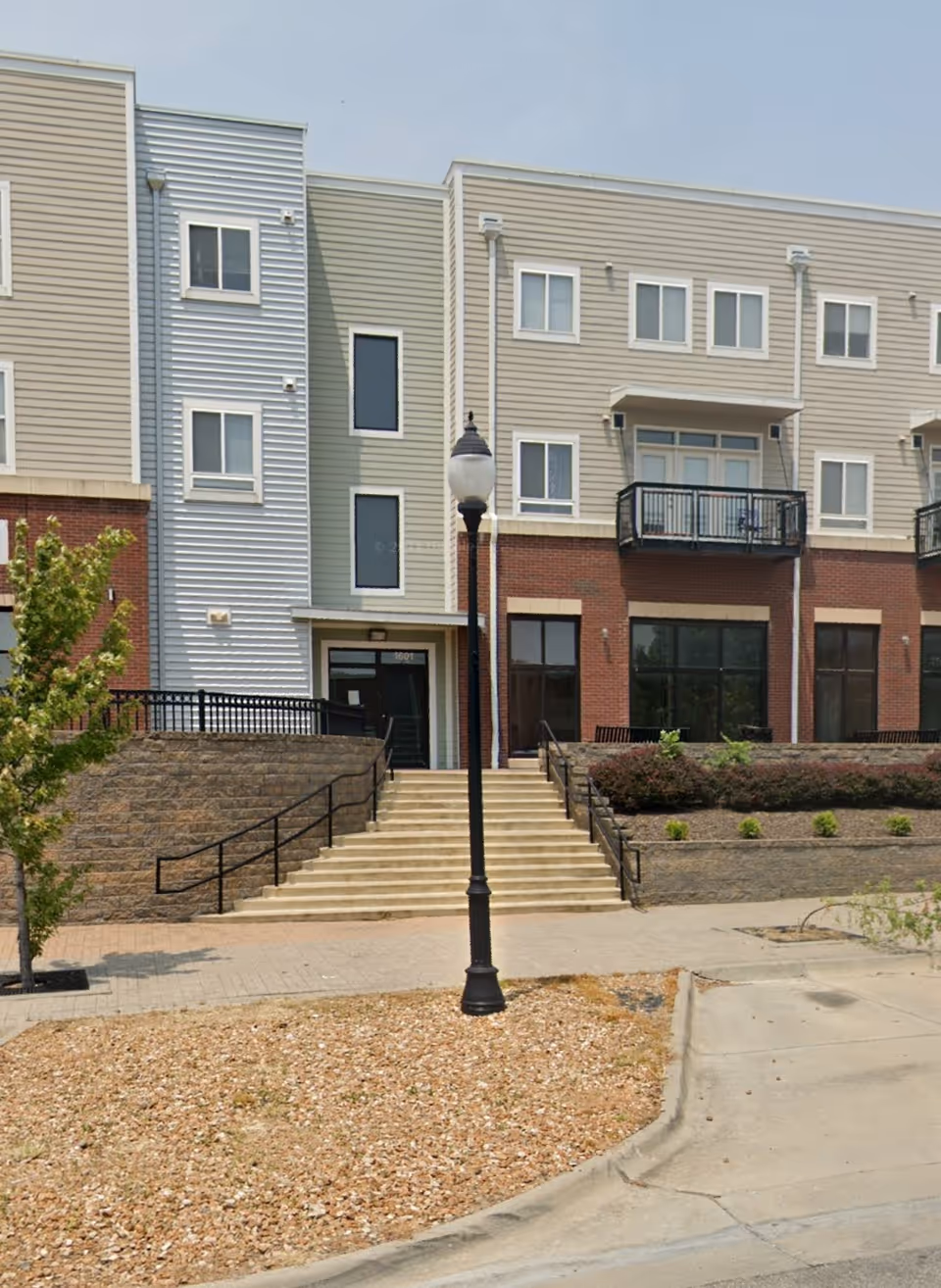 Front exterior view of a modern senior living building with stairs and a streetlamp.