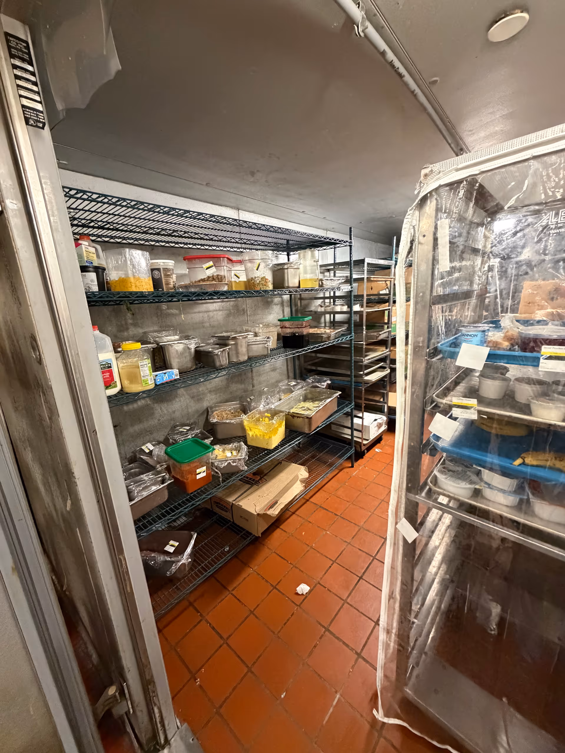 Industrial pantry area with metal shelves, labeled containers, and a glass-door refrigerator.