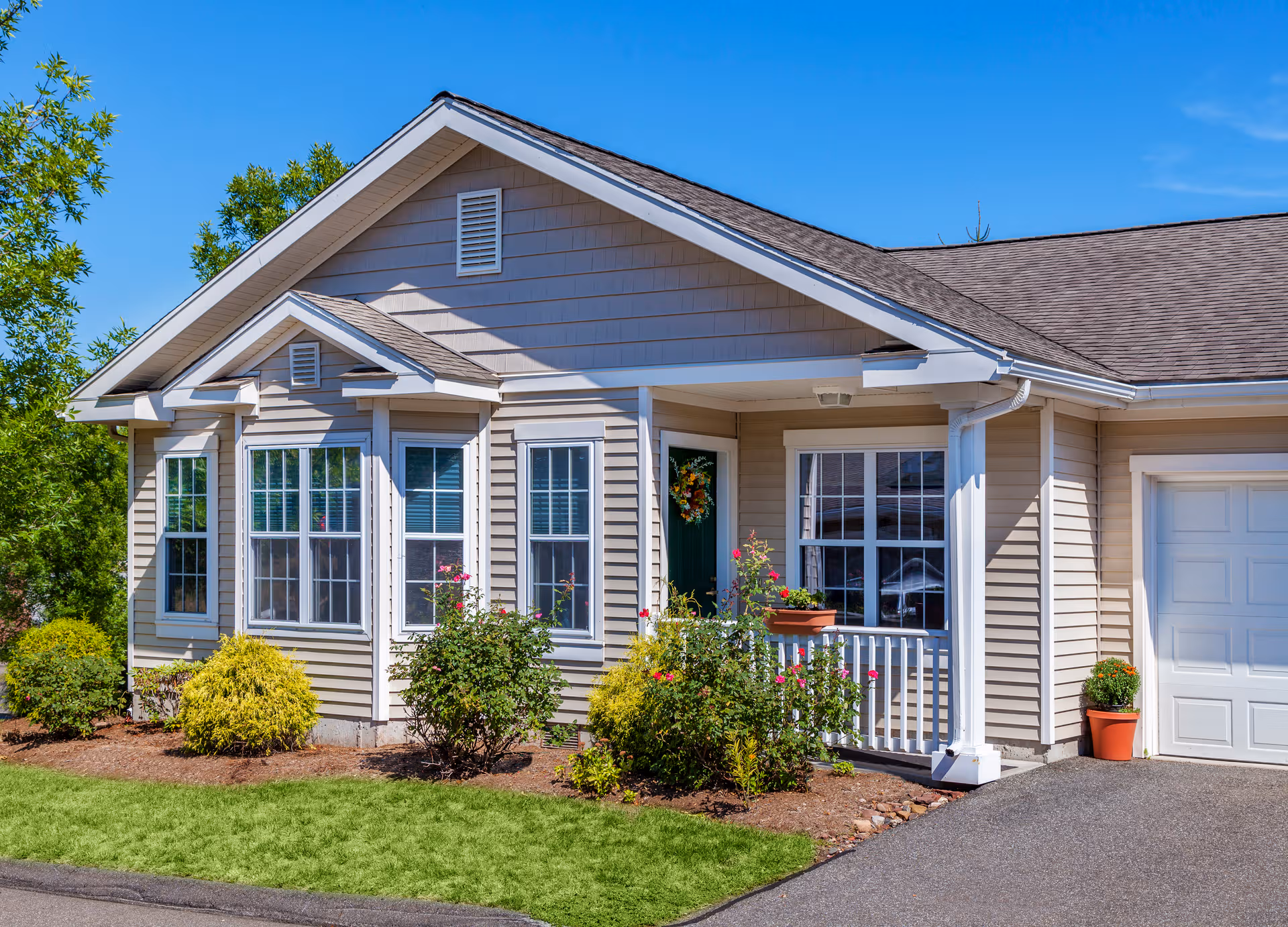 A beige single-story house with a covered porch and landscaped front yard.