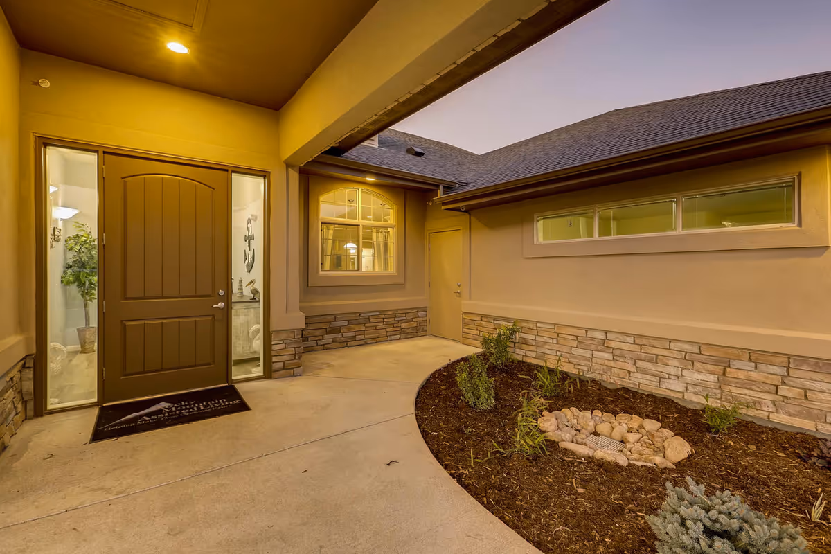 Entrance to a senior living facility with a brown door and landscaped walkway.