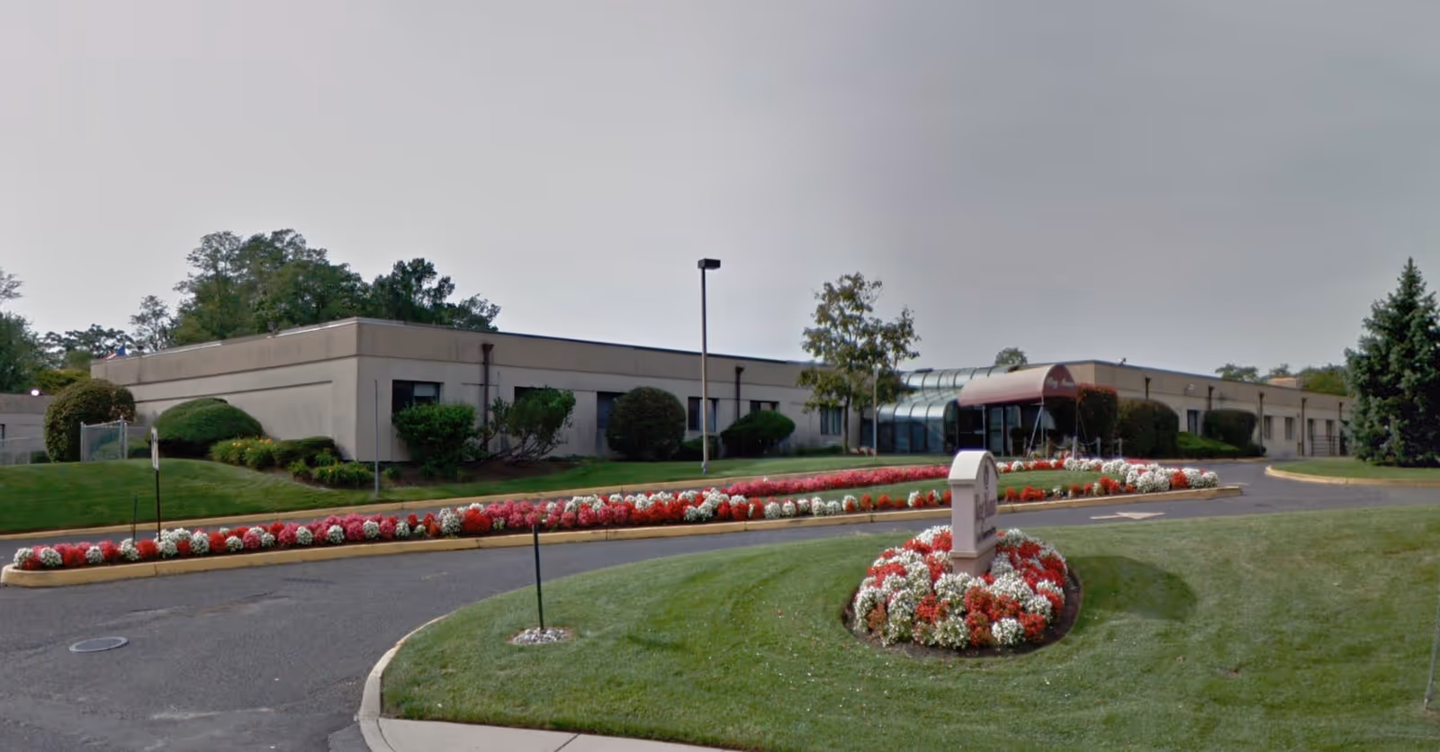 Single-story care center building with a glass-covered entrance, circular driveway, and landscaped flowerbeds in front.