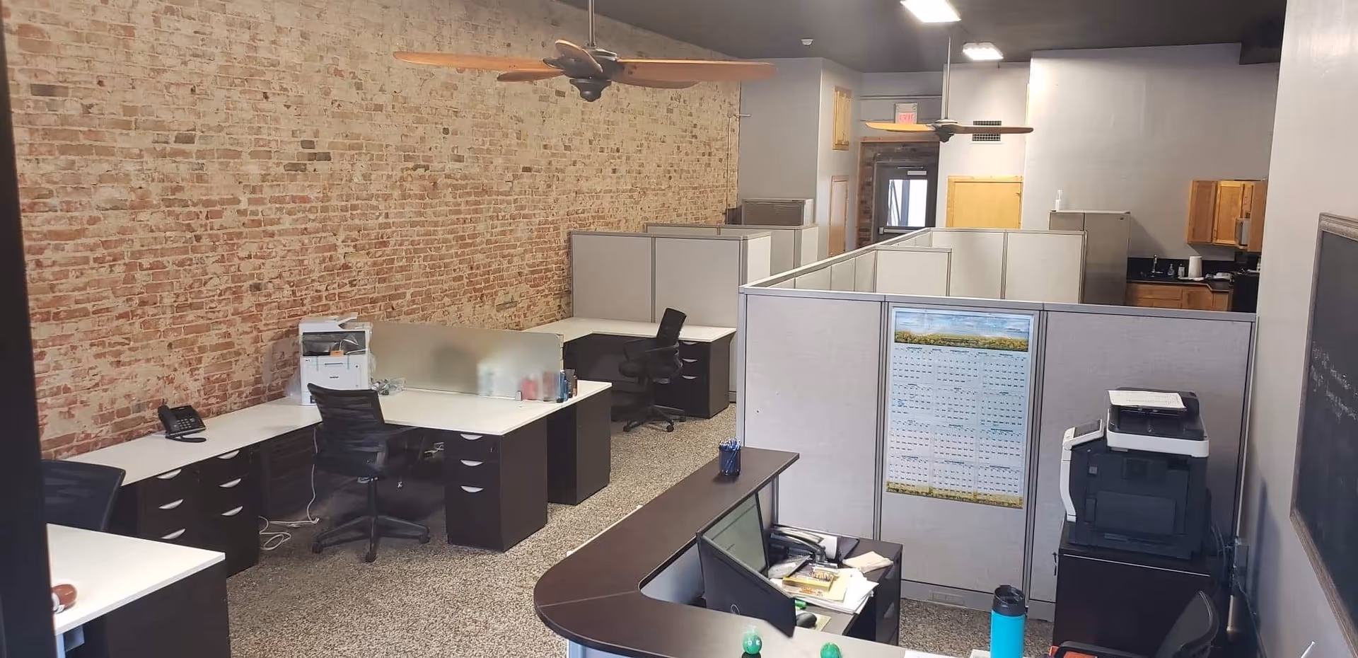 Open office area with cubicles, desks, and a brick wall in a hospice facility.