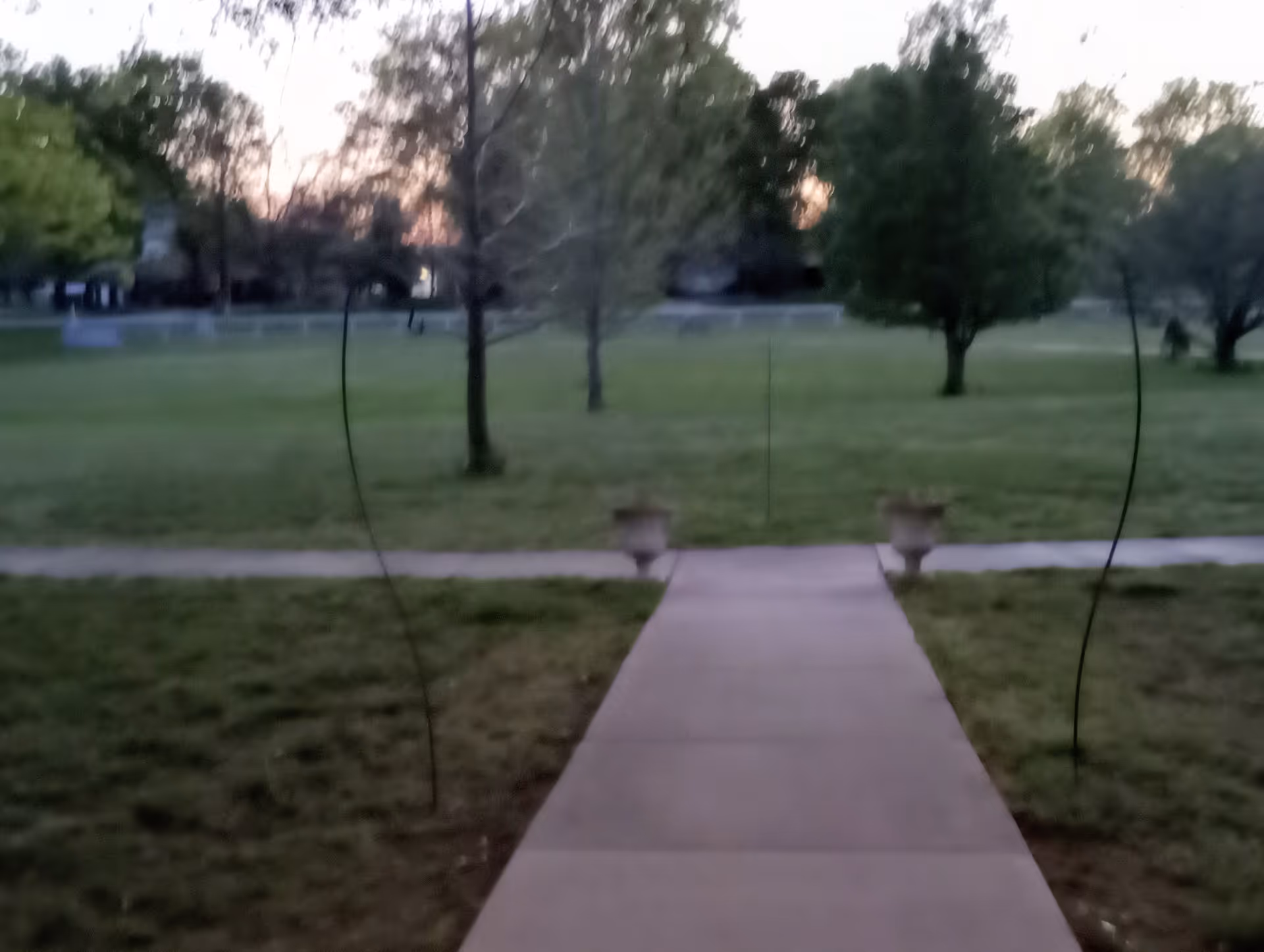 Blurred view of a concrete walkway through a grassy park at dusk
